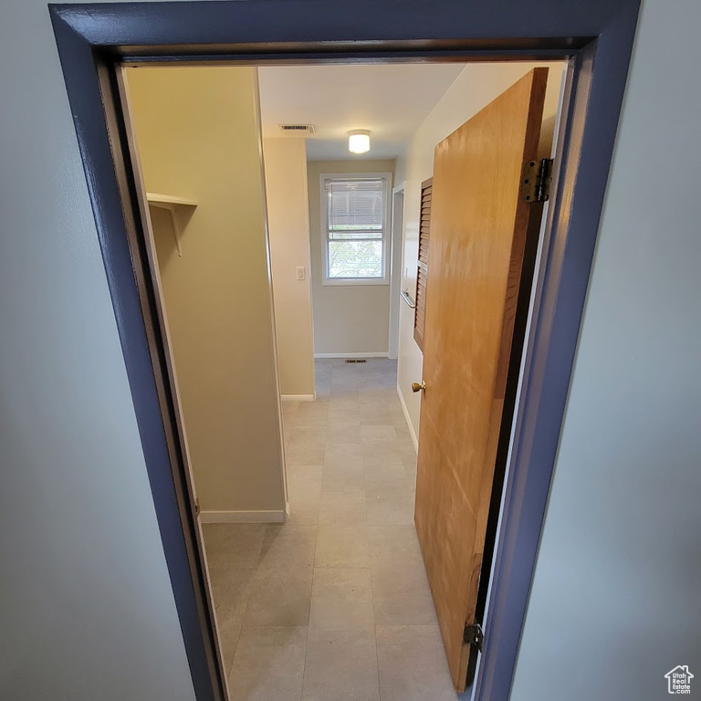 Hallway with light tile patterned floors, baseboards, and visible vents