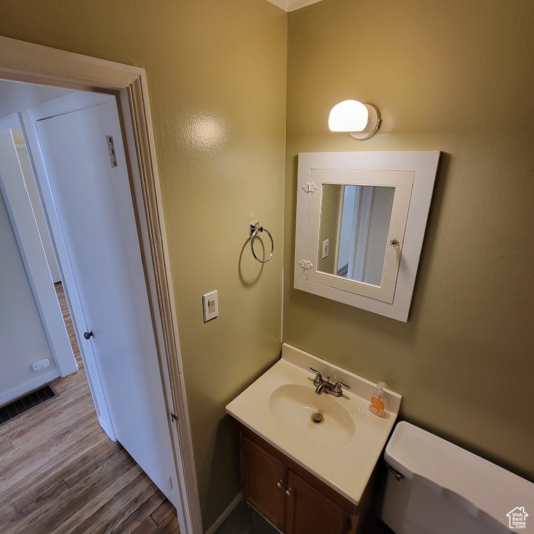 Half bath with vanity, toilet, wood finished floors, and visible vents