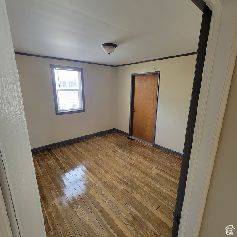 Spare room with wood-type flooring, baseboards, and crown molding