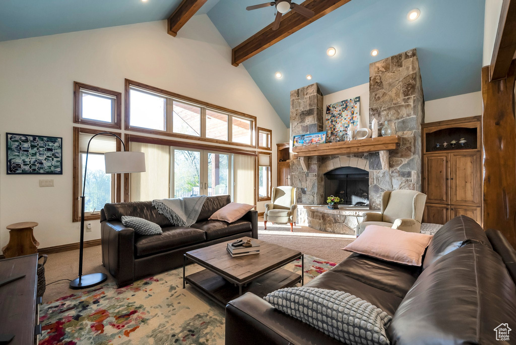 Carpeted living room featuring beam ceiling, high vaulted ceiling, a stone fireplace, a ceiling fan, and baseboards