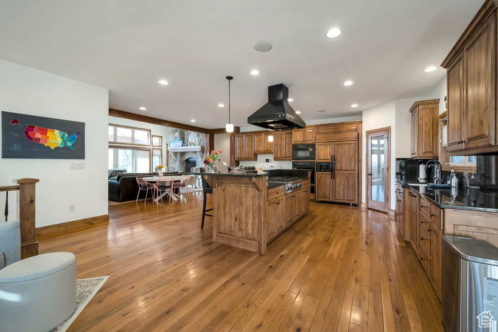 Kitchen with a kitchen island, light wood-style floors, a breakfast bar area, brown cabinets, and island exhaust hood
