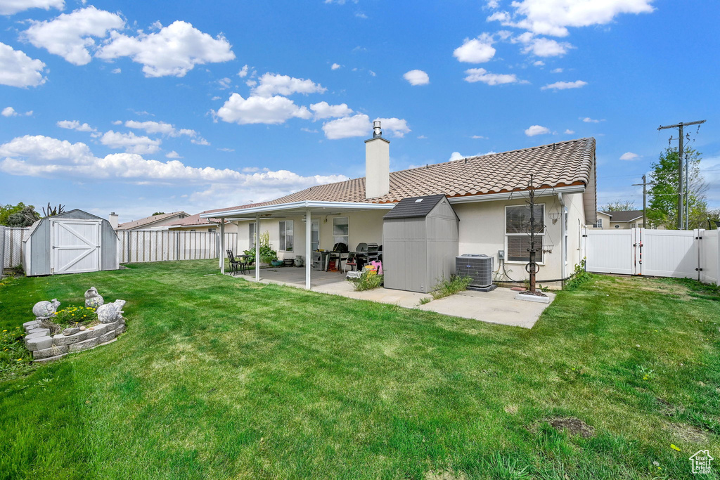 Back of house with a storage shed, a fenced backyard, a gate, a chimney, and a patio