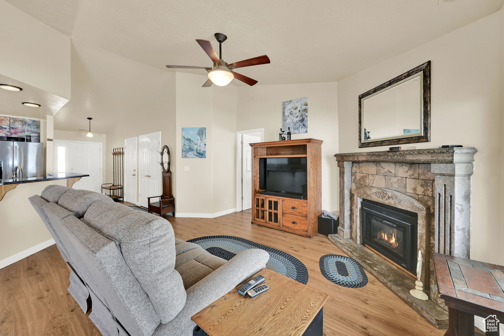 Living room featuring ceiling fan, a fireplace, baseboards, high vaulted ceiling, and light wood-style floors
