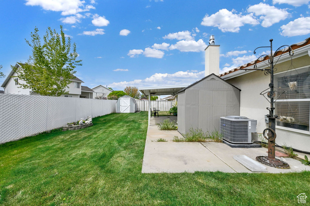 View of yard with a storage unit, a fenced backyard, an outbuilding, cooling unit, and a patio area