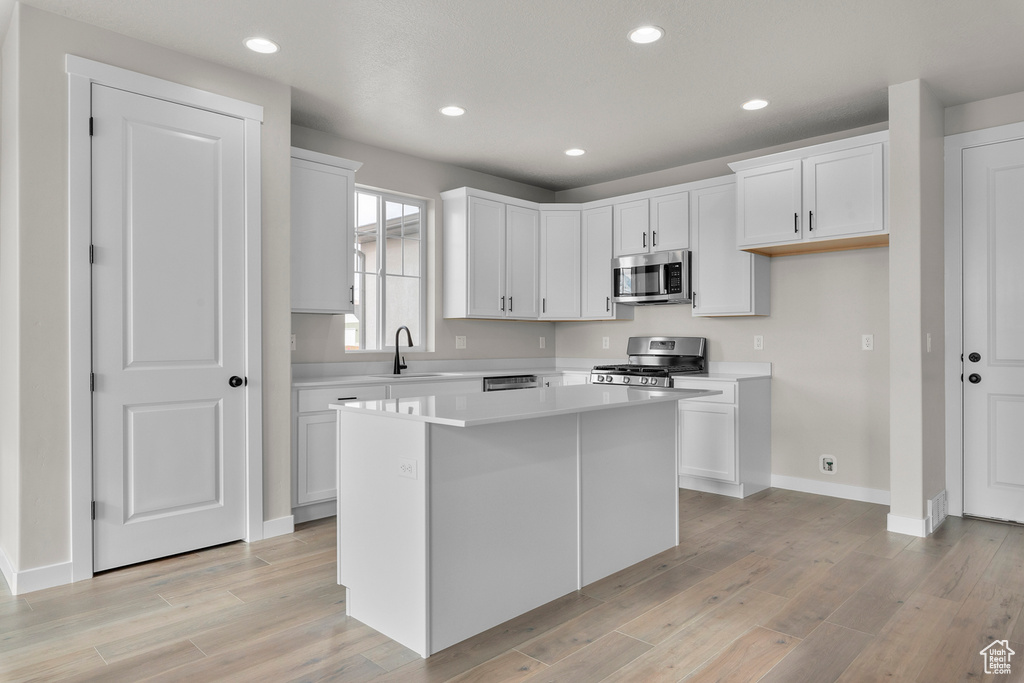 Kitchen with white cabinets, light countertops, light wood-style flooring, a center island, and stainless steel appliances