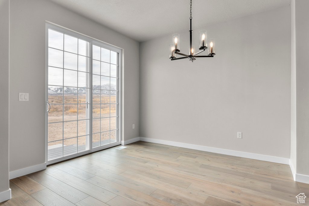 Empty room featuring baseboards, an inviting chandelier, and light wood finished floors