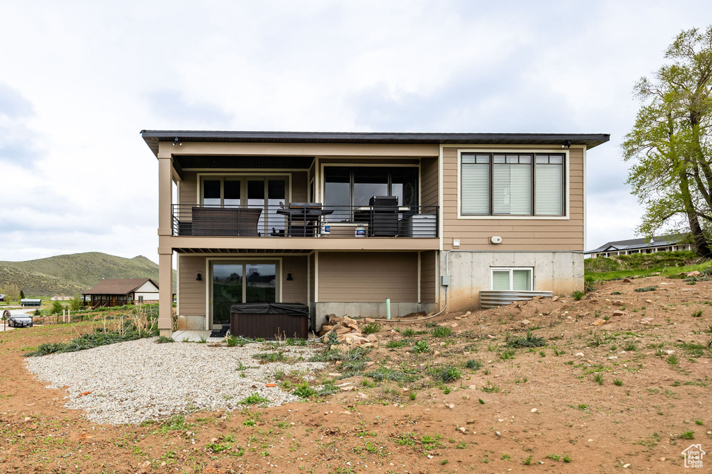Back of house with a hot tub, a balcony, and a mountain view