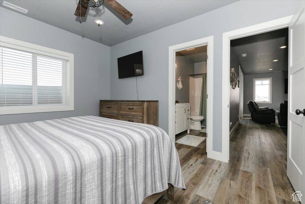 Bedroom with ceiling fan, ensuite bath, visible vents, wood finished floors, and baseboards