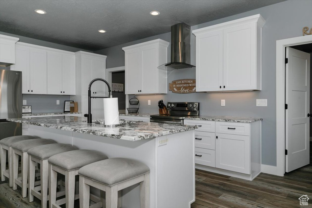 Kitchen with white cabinets, wall chimney range hood, appliances with stainless steel finishes, recessed lighting, and dark wood-type flooring