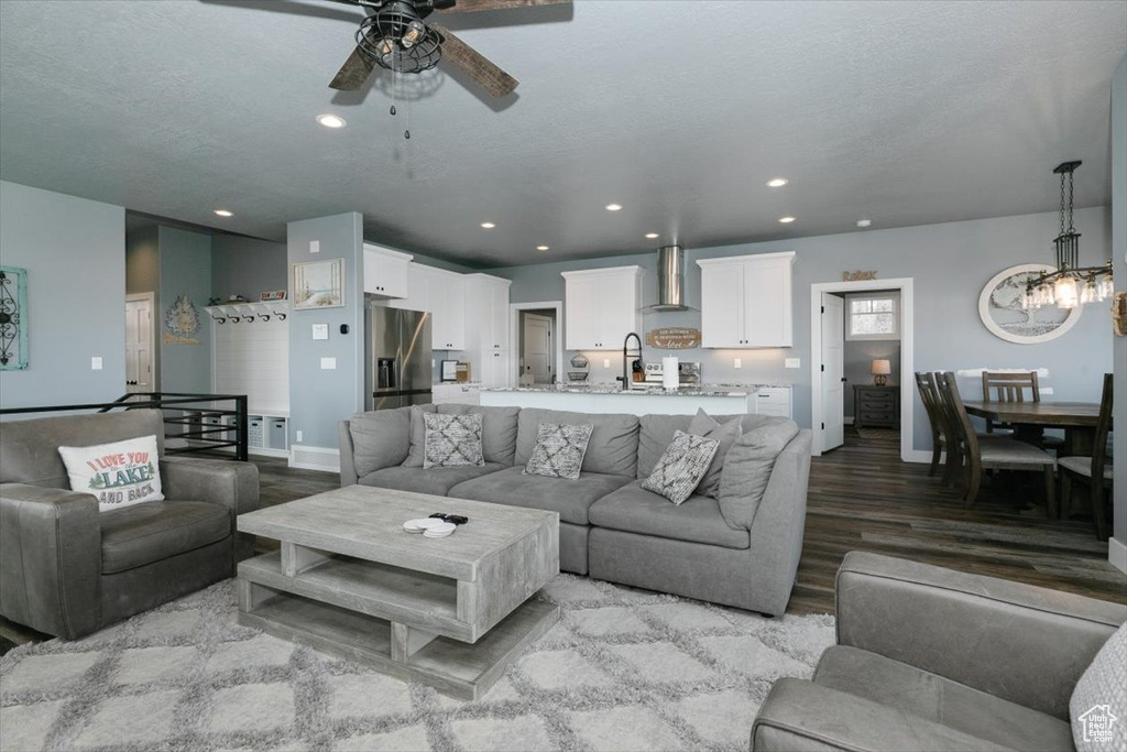 Living room with baseboards, recessed lighting, wood finished floors, and ceiling fan with notable chandelier