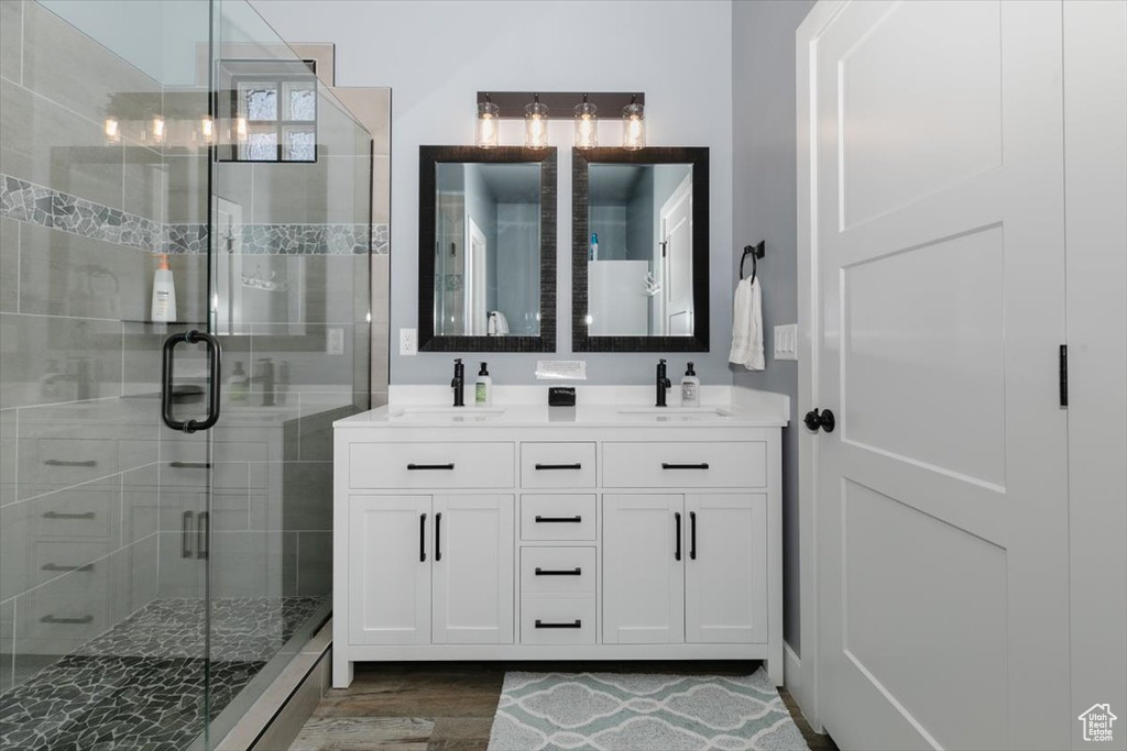 Bathroom with a shower stall, double vanity, a sink, and wood finished floors