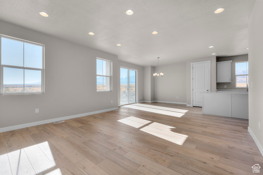 Unfurnished living room featuring an inviting chandelier, light wood-type flooring, recessed lighting, and visible vents