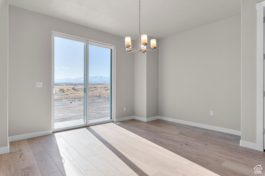 Spare room featuring baseboards, a notable chandelier, a mountain view, and light wood-style flooring