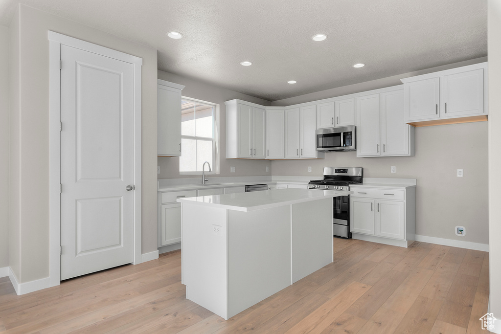 Kitchen featuring a kitchen island, light wood-style floors, light countertops, a sink, and appliances with stainless steel finishes
