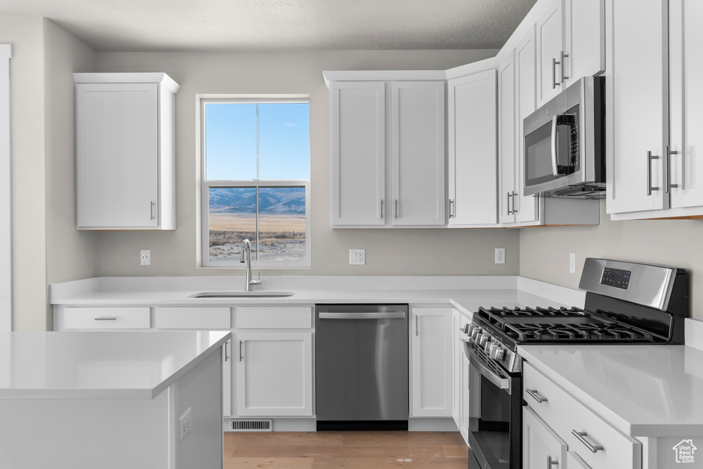 Kitchen featuring a sink, appliances with stainless steel finishes, white cabinets, and visible vents