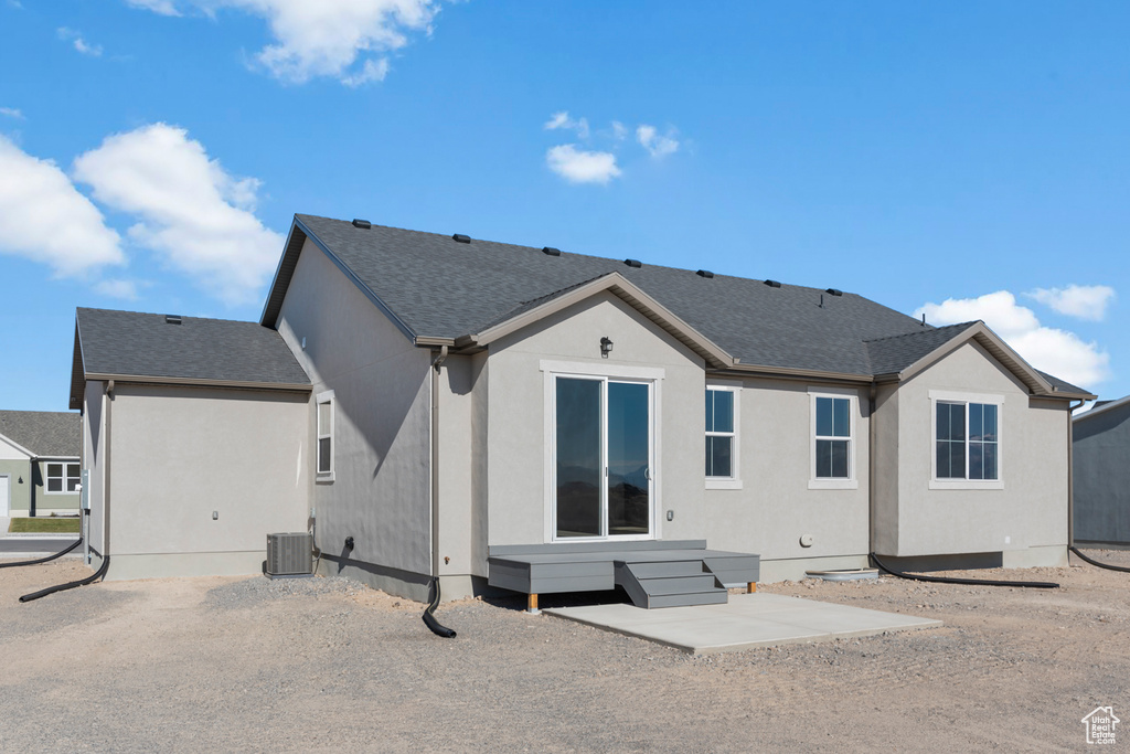 Back of property with central AC unit, roof with shingles, and stucco siding