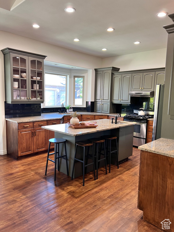 Kitchen featuring an island with sink, a kitchen bar, under cabinet range hood, backsplash, and stainless steel appliances