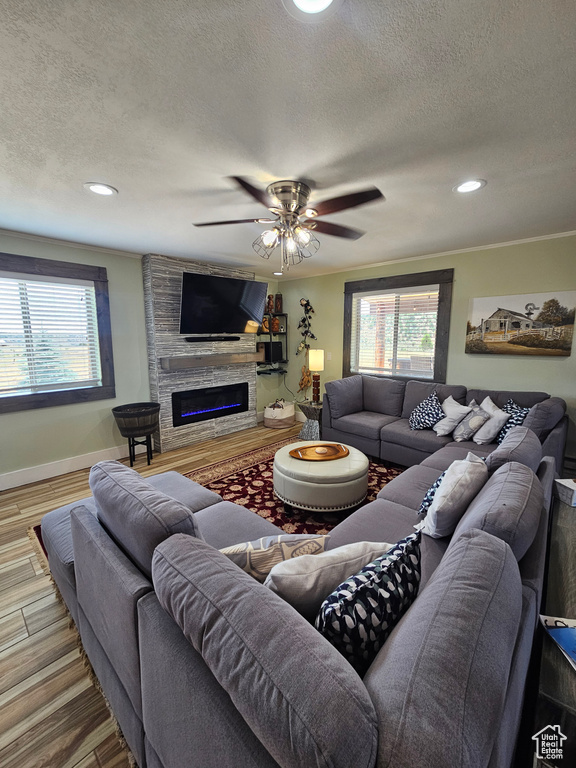 Living room with a ceiling fan, a textured ceiling, a stone fireplace, and baseboards