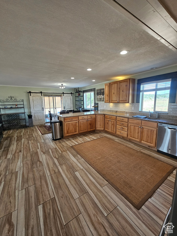 Kitchen with wood finish floors, a barn door, a textured ceiling, a peninsula, and stainless steel dishwasher