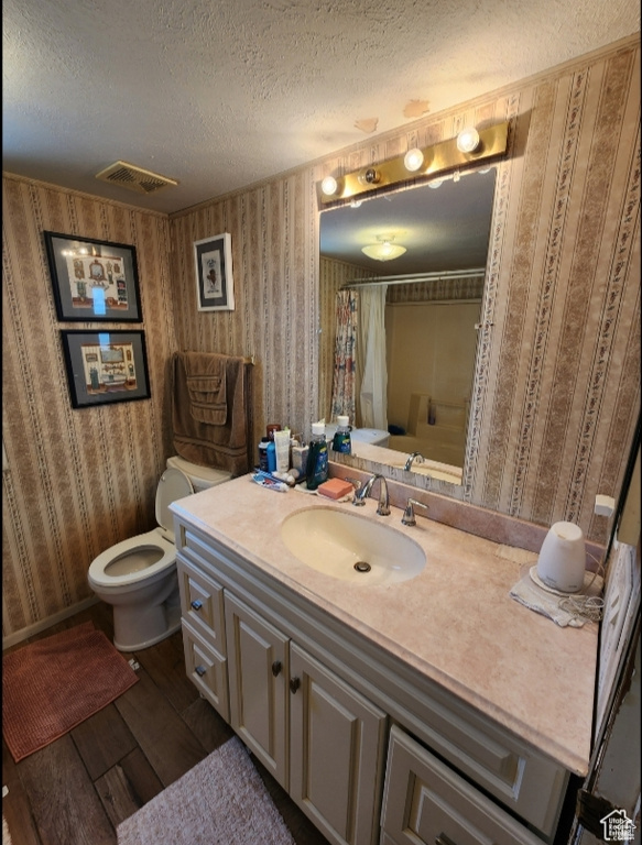 Full bathroom with vanity, toilet, a textured ceiling, wallpapered walls, and wood finished floors