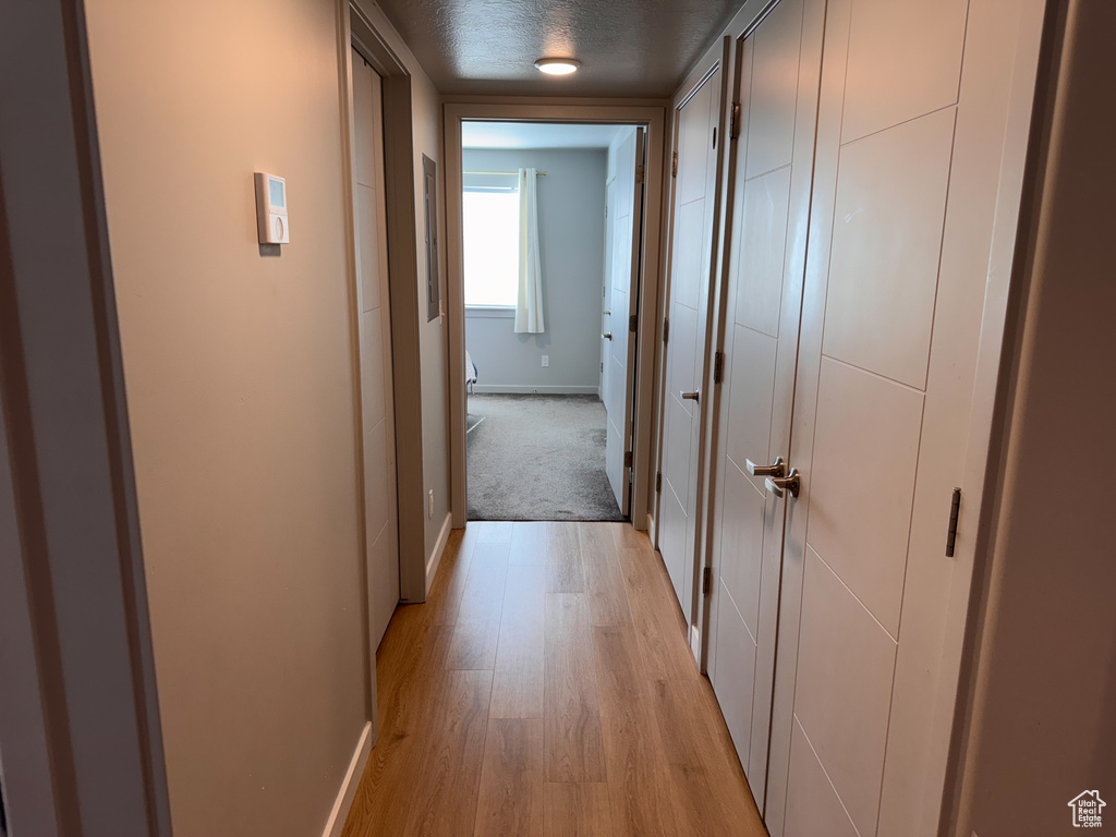 Corridor with baseboards, a textured ceiling, and light wood finished floors