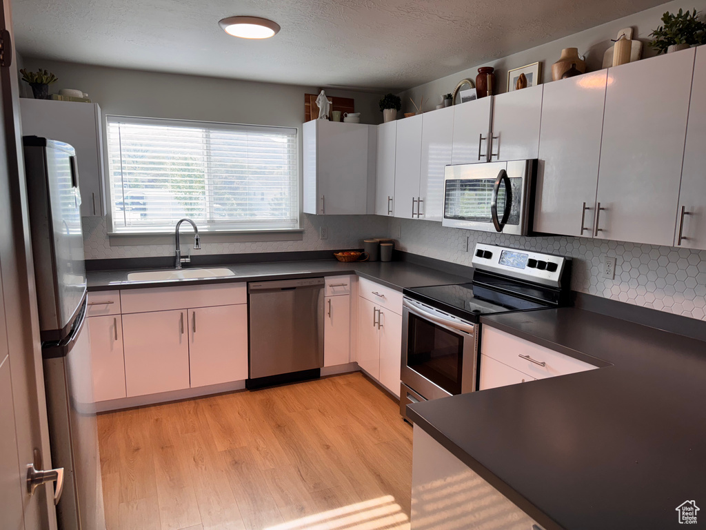 Kitchen with a sink, light wood-style floors, backsplash, dark countertops, and appliances with stainless steel finishes