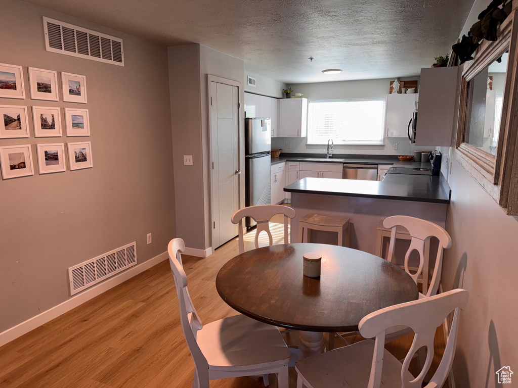 Dining room with a textured ceiling, visible vents, baseboards, and light wood-style floors