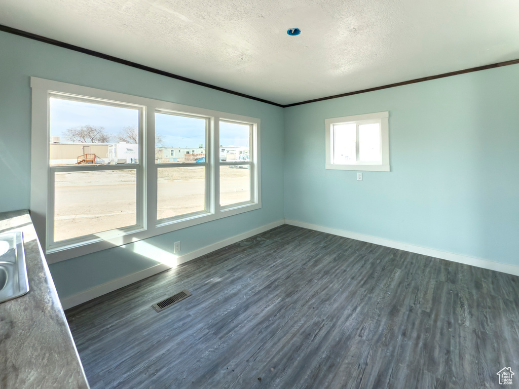Spare room featuring a textured ceiling, baseboards, visible vents, and dark wood-style floors