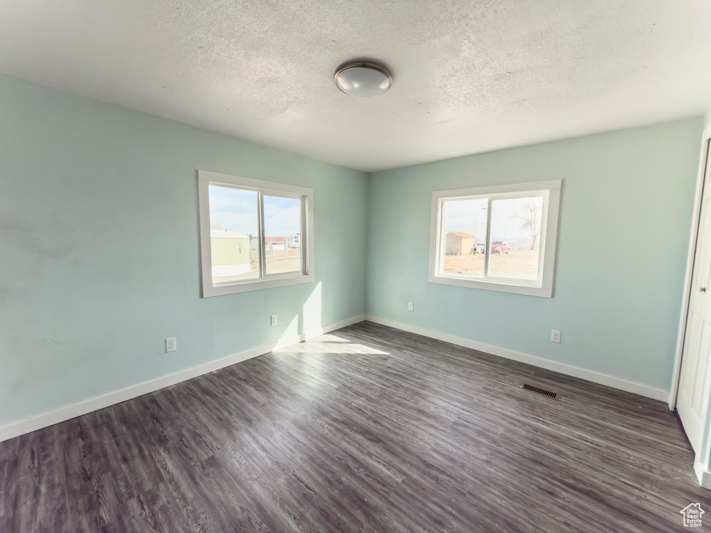 Unfurnished bedroom with a textured ceiling, visible vents, dark wood-style floors, and baseboards