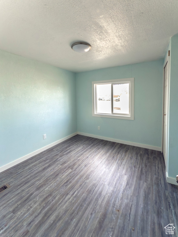 Unfurnished bedroom with baseboards, a textured ceiling, dark wood finished floors, and visible vents