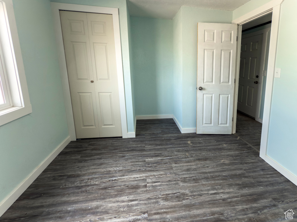 Unfurnished bedroom featuring baseboards, a closet, and dark wood-style floors