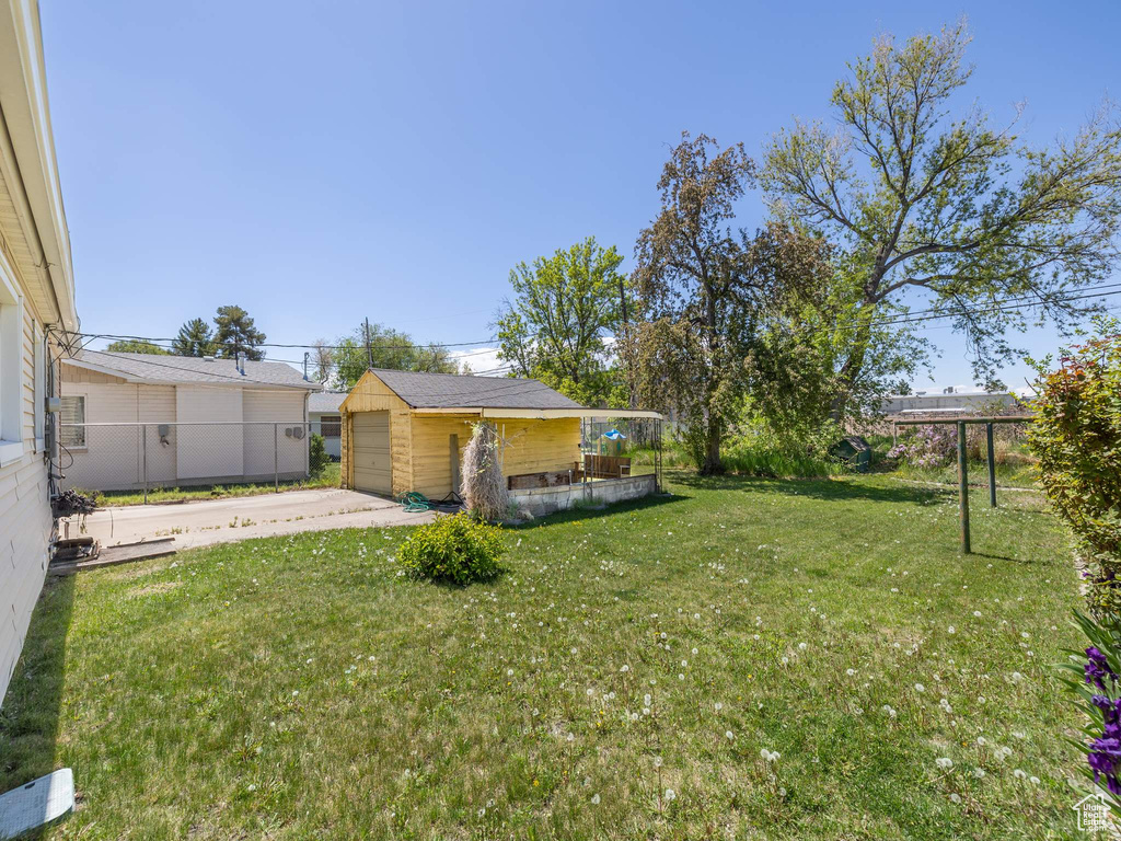 View of yard featuring concrete driveway, fence, an outdoor structure, and a garage