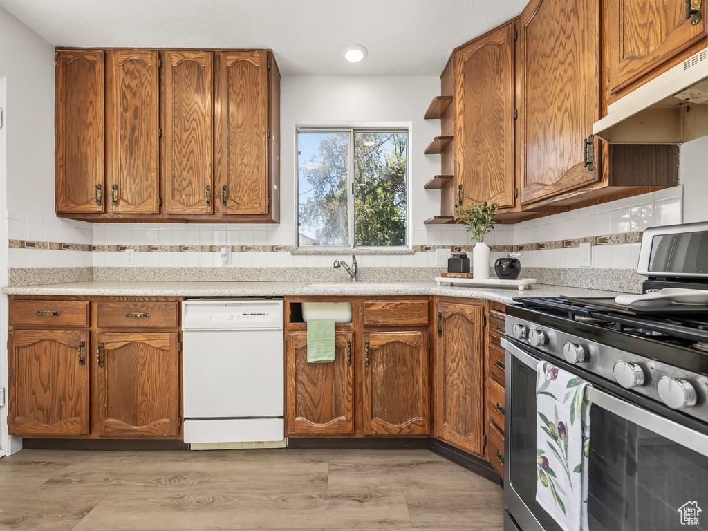 Kitchen with decorative backsplash, white dishwasher, stainless steel gas range oven, a sink, and under cabinet range hood