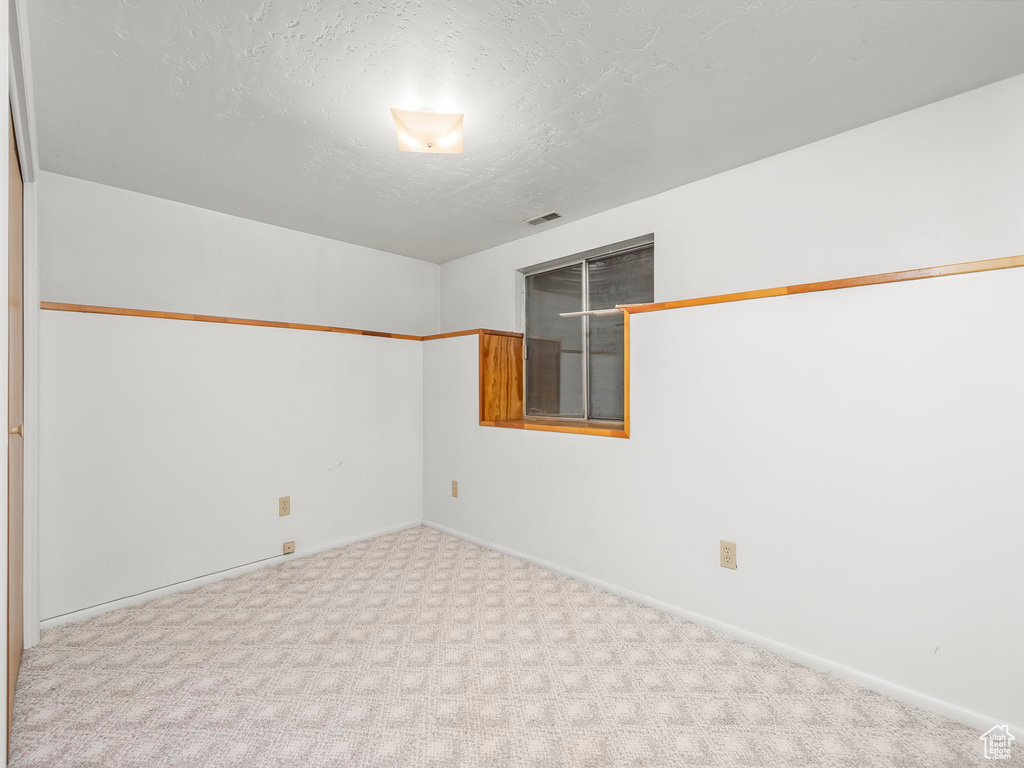 Carpeted spare room featuring baseboards, a textured ceiling, and visible vents