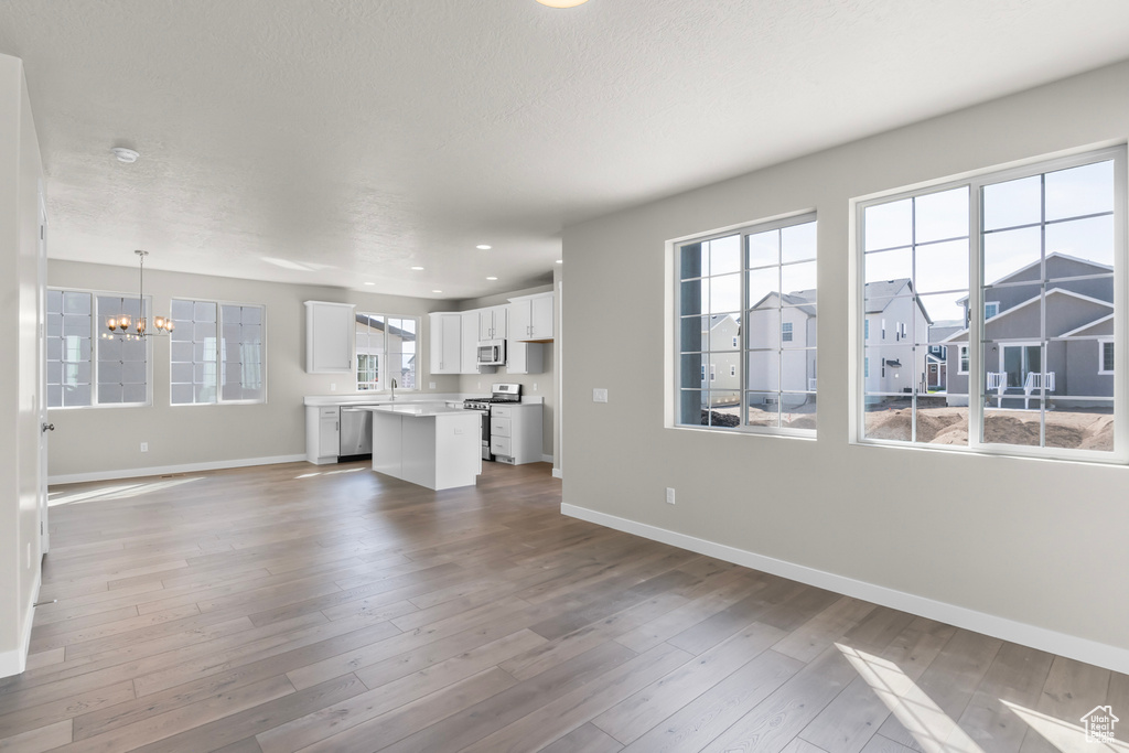 Unfurnished living room with a sink, baseboards, wood-type flooring, a notable chandelier, and recessed lighting