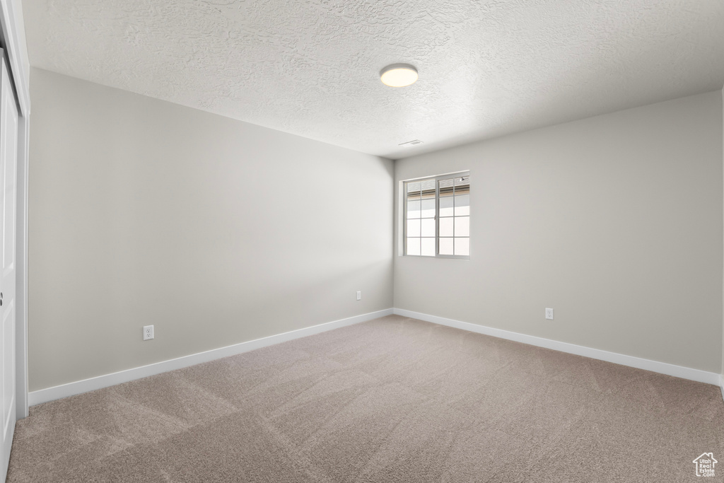 Spare room featuring baseboards, a textured ceiling, and light colored carpet