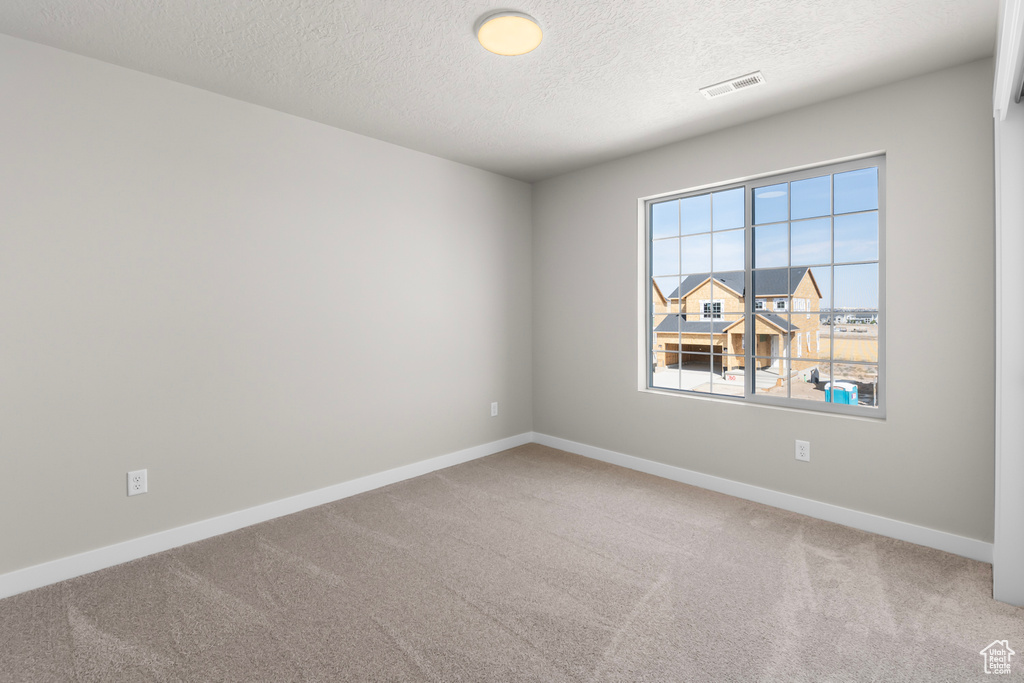 Carpeted spare room with baseboards, a textured ceiling, and visible vents