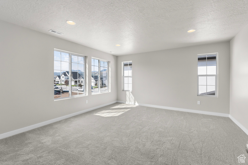 Carpeted spare room featuring visible vents, recessed lighting, a textured ceiling, and baseboards