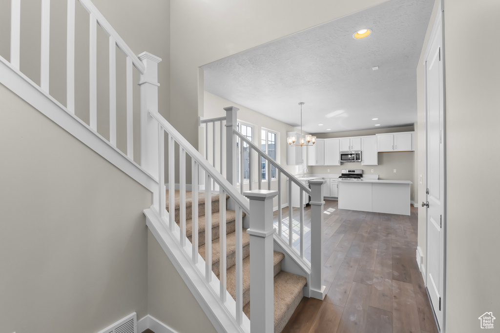 Stairway featuring an inviting chandelier, a textured ceiling, hardwood / wood-style floors, recessed lighting, and baseboards