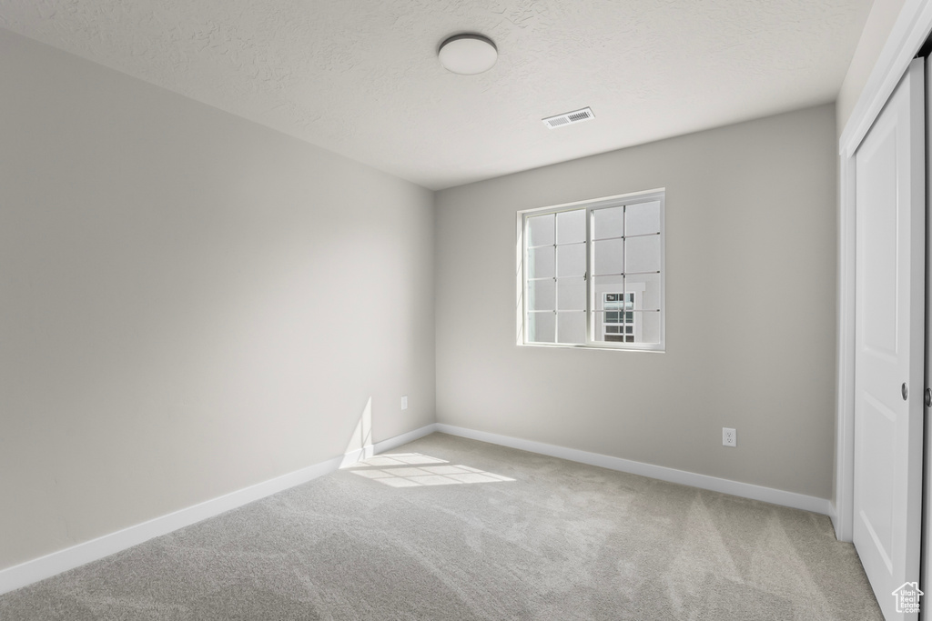 Unfurnished bedroom with a textured ceiling, visible vents, light colored carpet, baseboards, and a closet