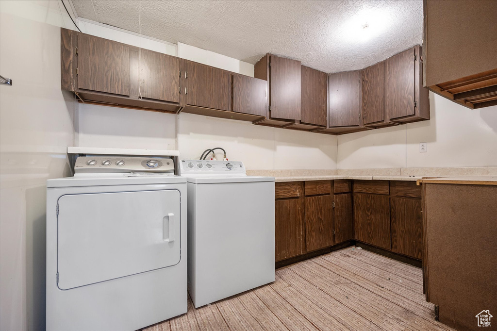 Washroom with cabinet space, a textured ceiling, light wood finished floors, and washer and dryer