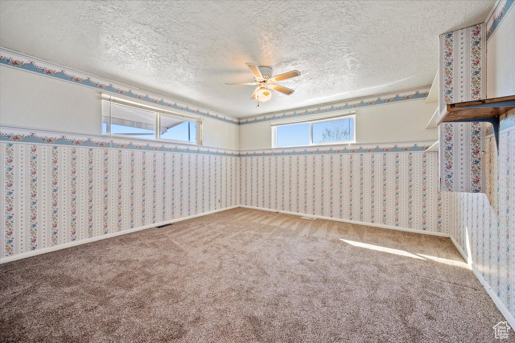 Carpeted empty room with a ceiling fan and a textured ceiling