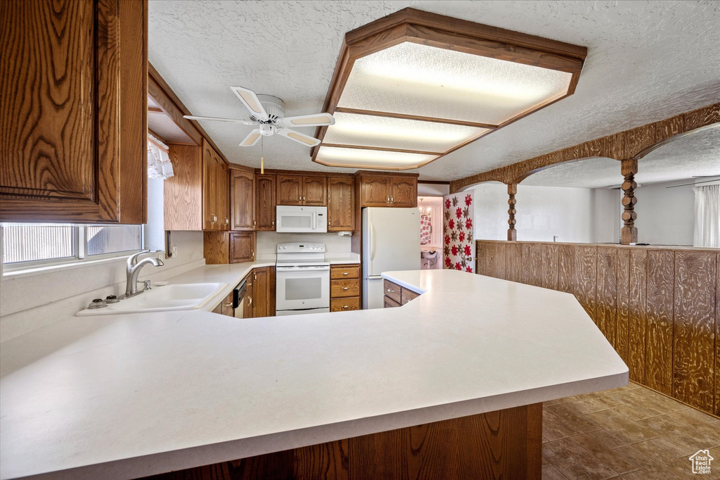 Kitchen with a ceiling fan, a textured ceiling, a sink, light countertops, and white appliances