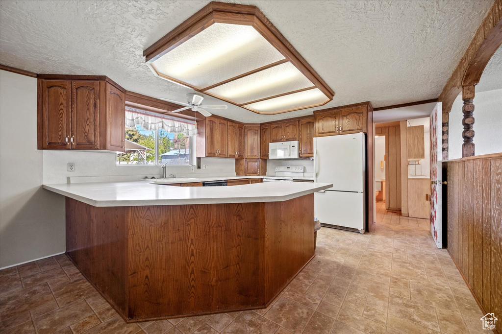 Kitchen featuring a peninsula, white appliances, light countertops, a textured ceiling, and a sink