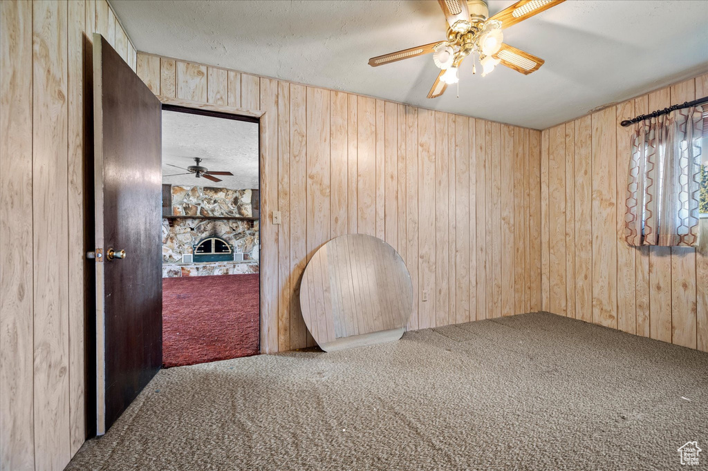 Spare room featuring ceiling fan, a textured ceiling, a stone fireplace, wooden walls, and carpet