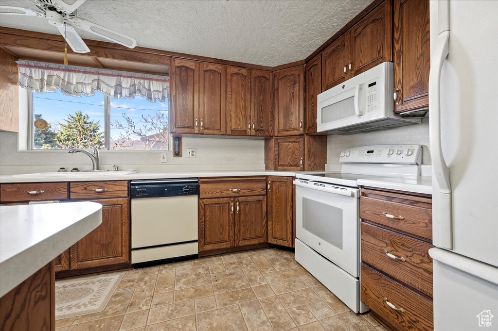 Kitchen with brown cabinetry, a ceiling fan, white appliances, light countertops, and a sink