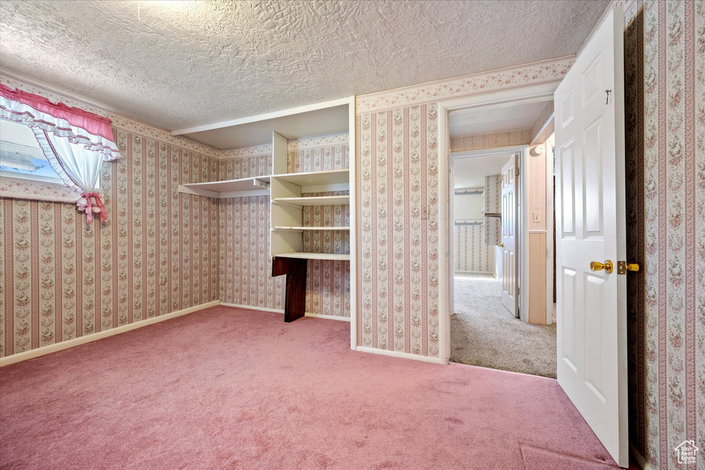 Unfurnished bedroom with a textured ceiling, wallpapered walls, and carpet