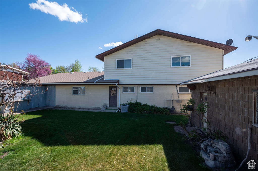 Rear view of house featuring brick siding, fence, a yard, and cooling unit