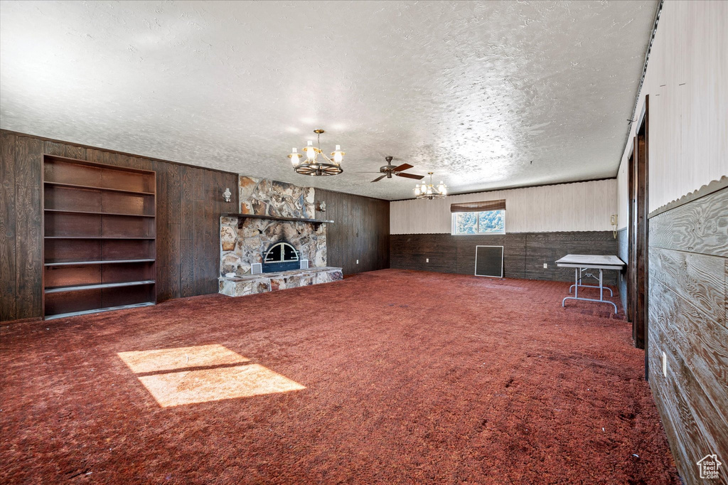 Unfurnished living room with carpet, wood walls, a textured ceiling, and a chandelier
