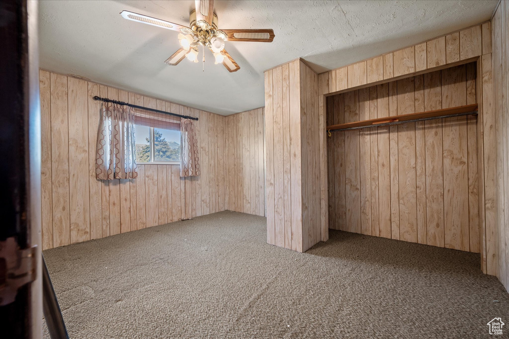Unfurnished bedroom with a closet, carpet flooring, ceiling fan, and wood walls